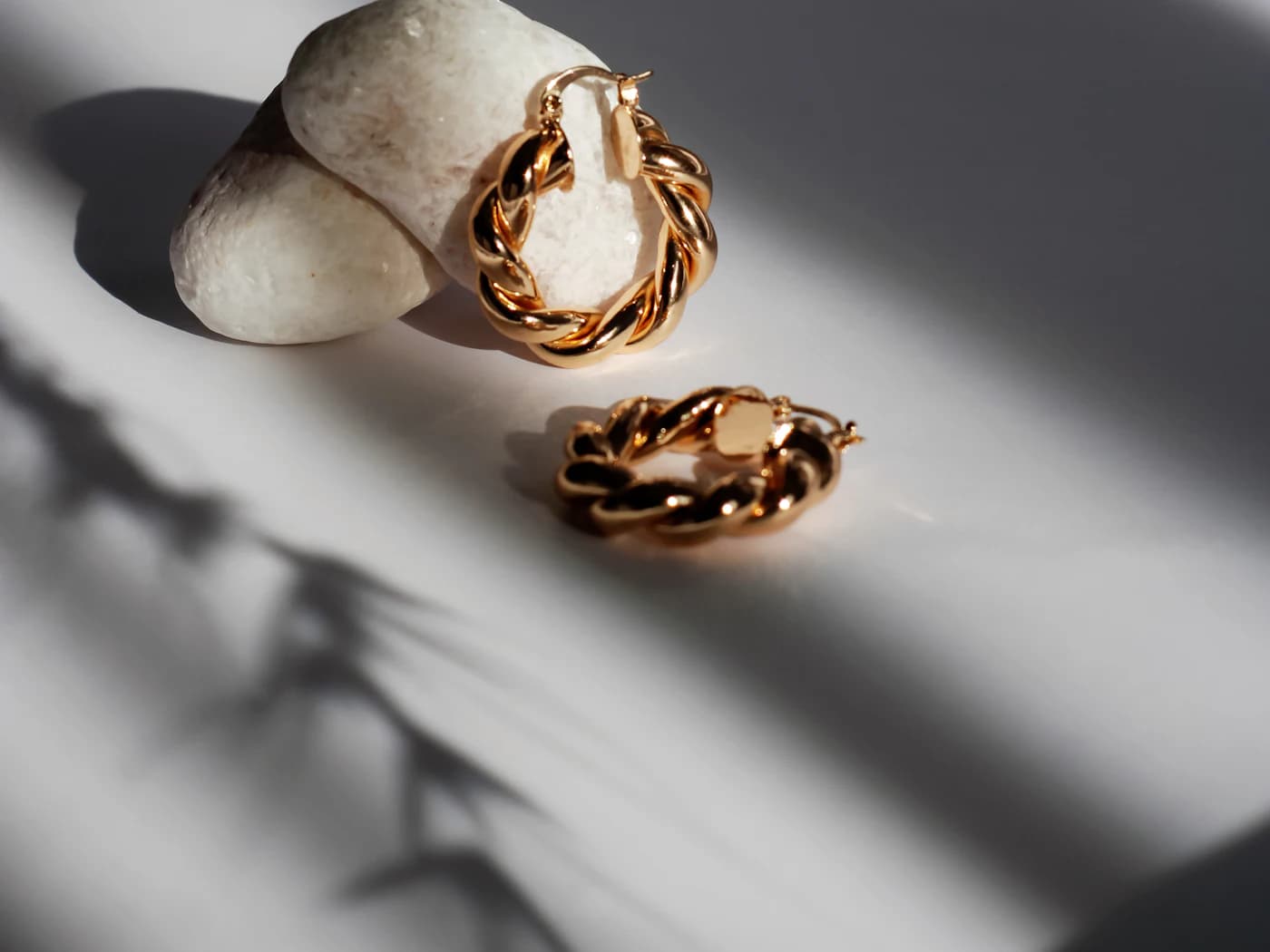 Twisted gold hoop earrings resting on white stone (illustrative photo)