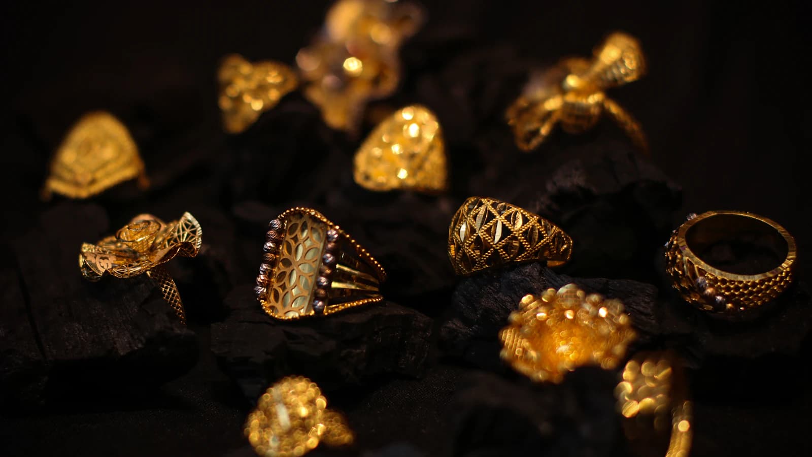 Ornate gold rings resting on dark charcoal pieces (illustrative photo)